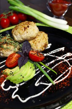 Fried cutlets with zucchini and tomatoes laid out on a black plate