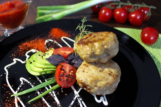 On a black plate zucchini with fried cutlets are beautifully decorated with mayonnaise and herbs with seasoning