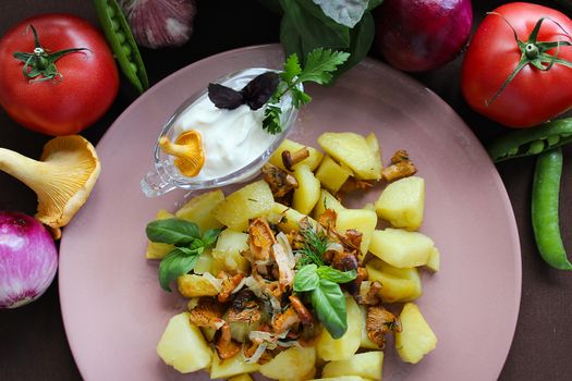 On the table in a plate fried chanterelles with onions and homemade potatoes with herbs