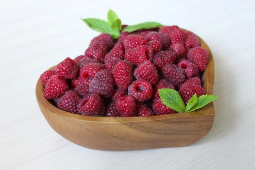 Garden sweet raspberries in a wooden container in the form of a heart