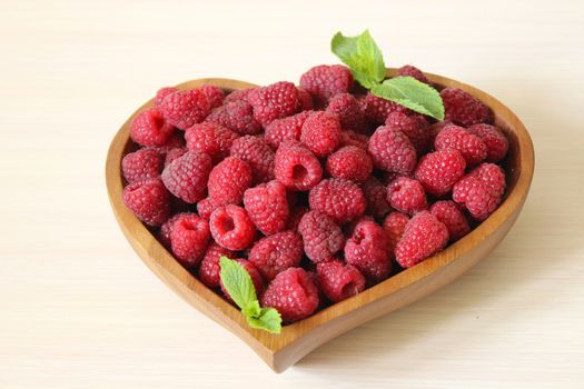 Ripe raspberries in a wooden container in the form of a heart