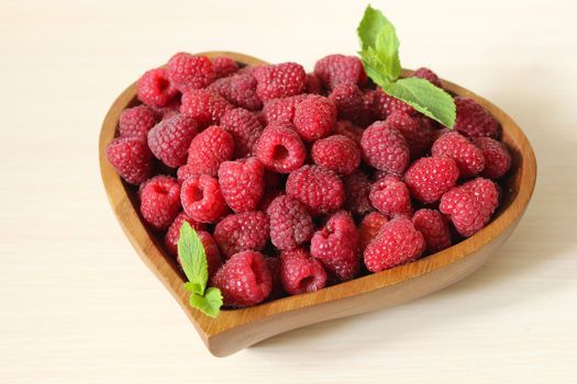 Close up of a ripe raspberry decorated with a mint leaf on a white background