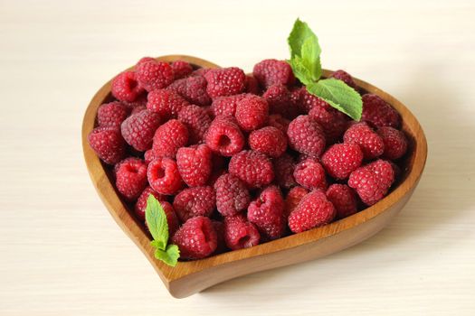 Garden raspberries in a wooden container decorated with a mint leaf on a white background