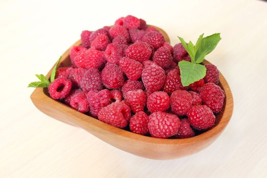Sweet ripe raspberries are decorated with a mint leaf on a white background
