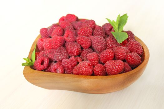 A raspberry berry on a wooden plate is decorated with a mint leaf on a white background