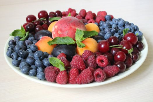 Summer mix of different berries on a light background on a white plate .Texture or background