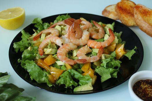 King prawn salad with lemon and herbs on a black plate