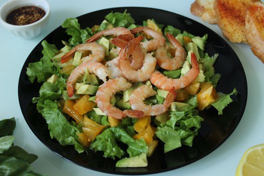 A dish of king prawns with toasted baguette and greens on a black plate.Texture or background