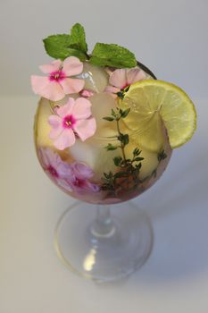 In a glass glass of chilled tea with a sprig of mint and flowers close up