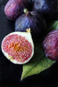 A slice of purple Fig with a green leaf on a dark background close-up.Texture or background