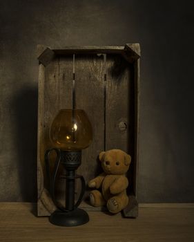 still life with old teddy bear and a golden light in an old wooden box on a table with dark background