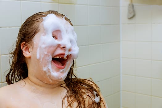 Happy little beautiful girl face swimming in the bathroom with water foam in bath