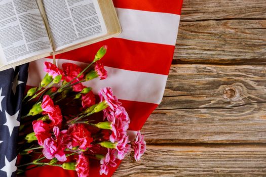 Los Angeles CA US 16 MAY 2020: Open reading Bible on a closeup of pink carnation of cut flowers in the American flag