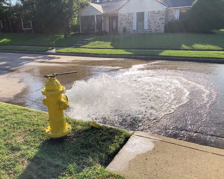 Opened yellow fire hydrant gushing water across a residential street near Dallas, Texas, America