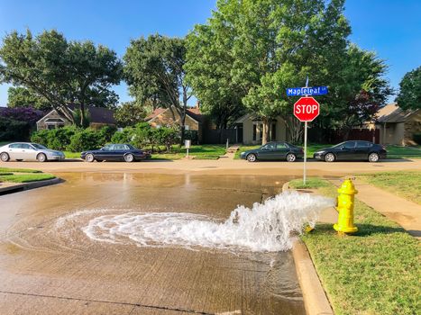 Typical neighborhood area with stop sign near Dallas, Texas, America with open yellow fire hydrant gushing water across a residential street. Row of suburban bungalow single family house behind