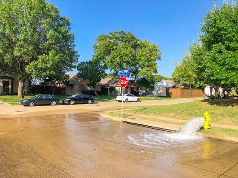 Typical neighborhood area with stop sign near Dallas, Texas, America with open yellow fire hydrant gushing water across a residential street. Row of suburban bungalow single family house behind