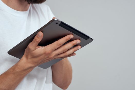 Tablet with a touch screen on a light background male hands white t-shirt cropped view. High quality photo