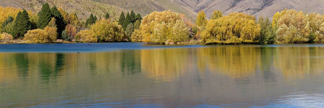 A scenic lake with yellow autumn foliage on the trees on the banks adding beautiful reflections to the calm water