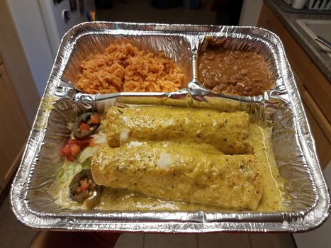 hand holding container of spicy enchiladas and rice and beans Mexican food