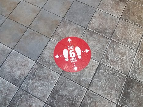 red please stay six feet apart sign on grey tiles on floor