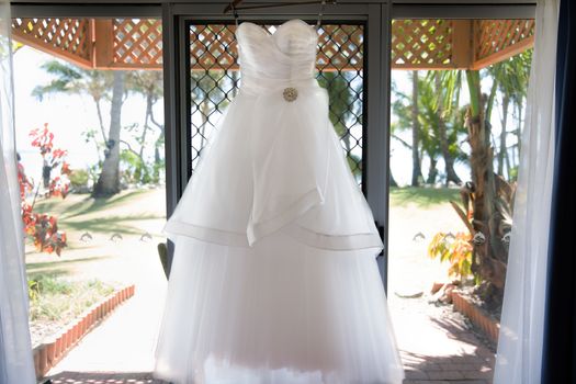 A Bride's wedding dress on hanger ready to be worn, framed by a window