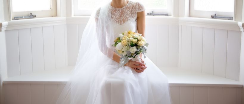 A bride holding her bouquet in dreamy soft window light as she poses before her wedding