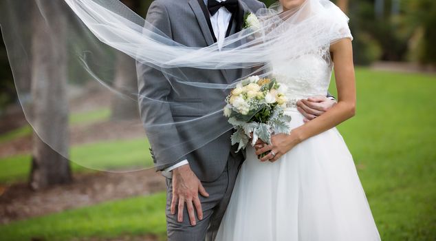 Newly married bride and groom pose with flowing veil in a garden