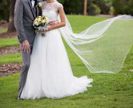 Newly married bride and groom pose with flowing veil in a garden