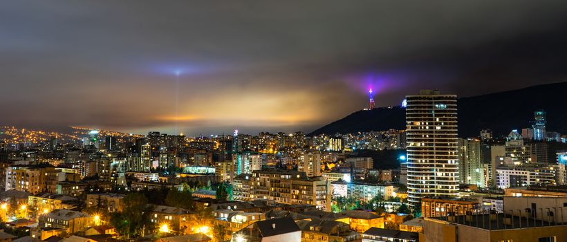Dramatic night sky with  light of Moon through the clouds over Tbilisi's downtown, capital city of Georgia