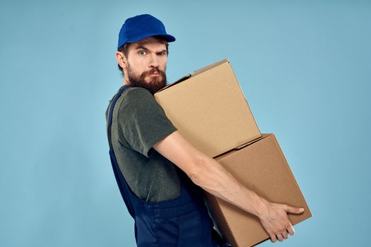 Man in working uniform with boxes in hands delivery service blue background. High quality photo