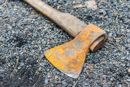 A rusty ax lies on the ground on fine gravel and pebbles