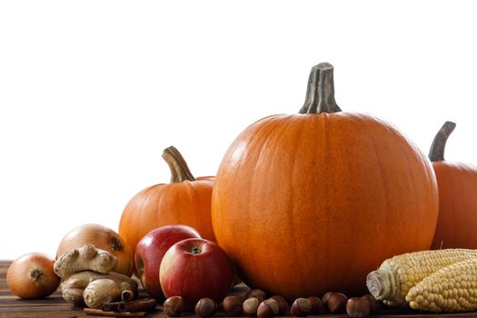 Autumn harvest still life with pumpkins, apples, hazelnut, corn, ginger, onion and cinnamon on wooden table isolated on white background