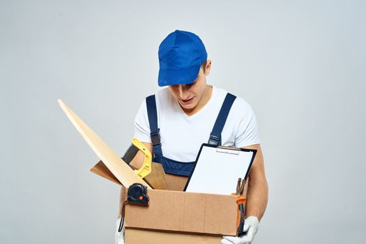 man in working uniform with a box in his hands tools loader delivery light background. High quality photo