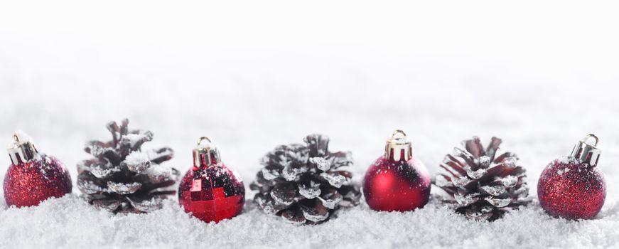 Winter Christmas decor of red christmas bauble ball row and pine cones in snow isolated on white background