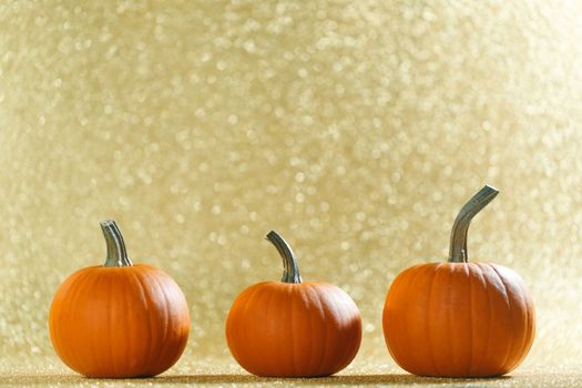 Three Pumpkins on golden glittery background with bokeh lights and copy space