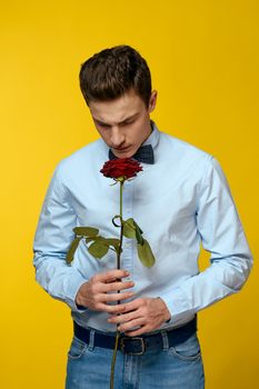 Elegant man in a suit with a red rose in his hands on a yellow background, cropped view. High quality photo