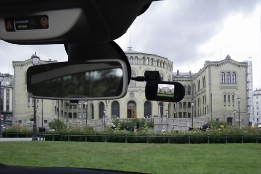 Looking through a dashcam car camera installed on a windshield with view of the facade of the Norwegian Parliament in Oslo, Norway