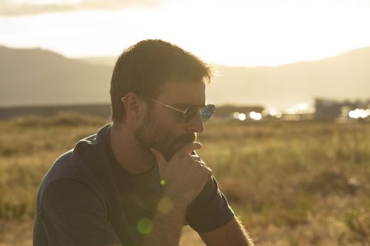 A young man, wearing glasses, concentrating on himself, meditates in a relaxed way, while enjoying the afternoon sun on a promenade in northern Spain.