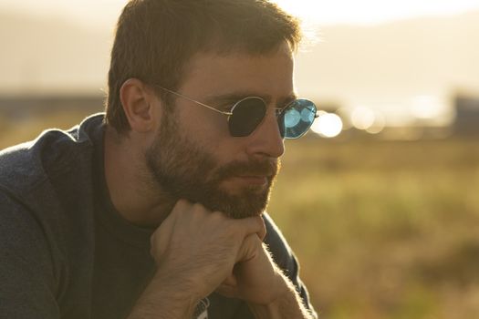 A young man, wearing glasses, concentrating on himself, meditates in a relaxed way, while enjoying the afternoon sun on a promenade in northern Spain.