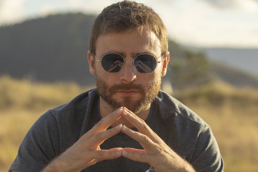 A young man, wearing glasses, concentrating on himself, meditates in a relaxed way, while enjoying the afternoon sun on a promenade in northern Spain.