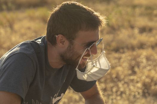 A young man laughs foolishly, as he hangs his protective face mask from his sunglasses.