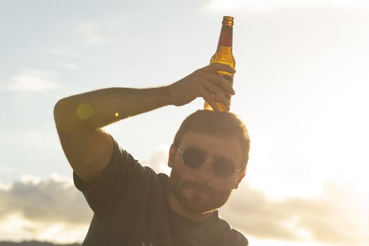 A young man, with glasses, does silly things, while drinking beer from a bottle, enjoying the sunset in Galicia, northern Spain.