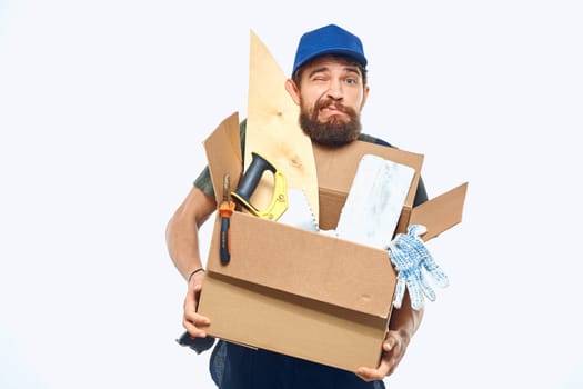 Worker man in uniform with a box in his hands tools delivery service light background. High quality photo