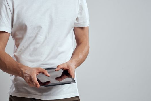 Tablet with a touch screen on a light background male hands white t-shirt cropped view. High quality photo