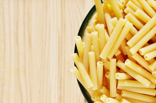 Pile of yellow pasta maccheroni in glass bowl on wooden table , dry pasta shaped like narrow tubes ,