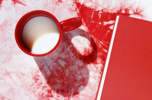 Red mug with milk on red-white cotton background , red closed book in the background ,