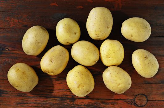 Whole yellow potatoes on red wooden table , uncooked and unpeeled vegetable