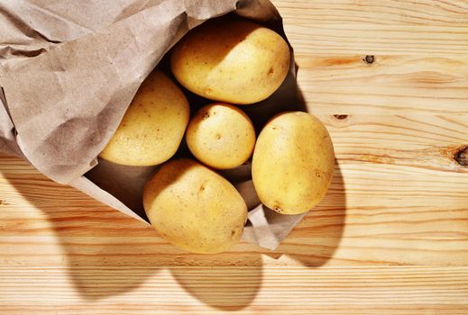 Whole yellow potatoes in bag on wooden table , uncooked and unpeeled vegetable