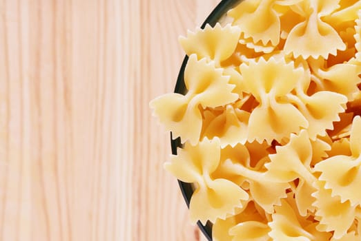 Dry pasta farfalle in glass bowl on wooden table , bow-tie pasta or butterfly pasta with two ruffled edges and the centre pinched together