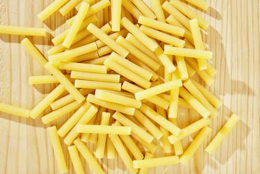 Pile of yellow pasta maccheroni on wooden table , dry pasta shaped like narrow tubes ,